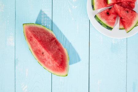 A top view of sliced watermelons on a blue wooden surface under sunlightの写真素材