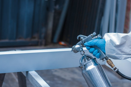 A closeup of a person wearing a protective suit and gloves spray painting in a workshopの写真素材
