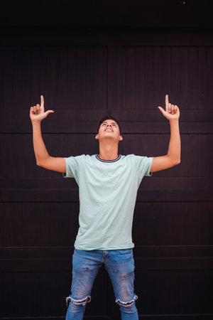 A vertical shot of a young Hispanic man thanking God against a black wall