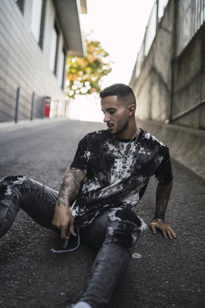 A hot tattooed stylish man wearing ripped jeans, a T-shirt with marble patterns and accessoriesの写真素材