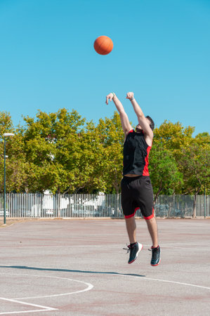 A vertical shot of a male throwing the basketball ball in a court