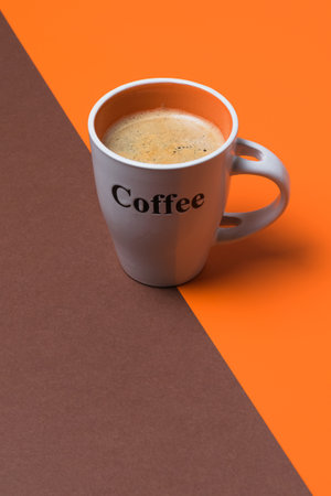 A vertical shot of a fresh coffee cup on orange and brown split backgroundの写真素材