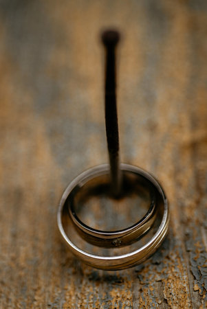 A vertical shot of silver wedding rings hanging on a nail against a wooden wallの写真素材