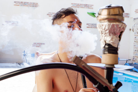A young male smoking a hookah next to the pool in summer