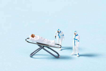 A closeup of toy healthcare providers helping a patient on a stretcher on a blue background - concept of treating COVID19 patientsの写真素材