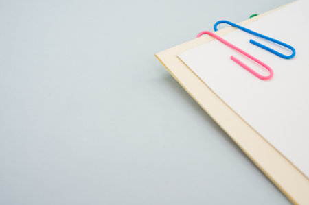 A closeup shot of a blank paper with colorful paper clips on a light green backgroundの写真素材