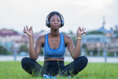 A shallow focus shot of an African female meditating while witting on the grass in a parkの写真素材