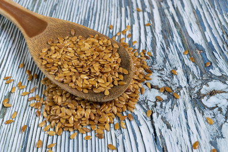 A view of golden flax seeds in a wooden spoon on a blue wooden tableの写真素材