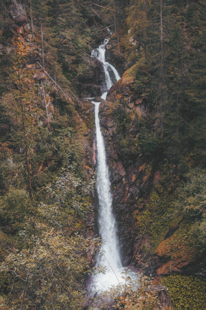 A majestic vertical shot of a tall long waterfall flowing over a rocky forested cliff surfaceの写真素材