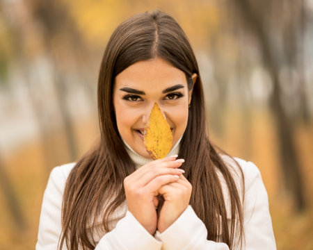 A Caucasian attractive woman smiling and holding a fallen leaf in the fallの写真素材