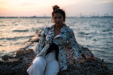 A shallow focus of a stylish female with her hair in a messy bun sitting on rocks surrounded by the...