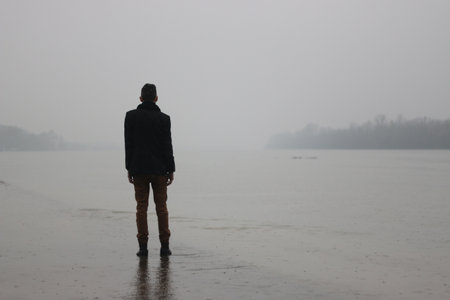 A man standing on the side of a river while rainingの写真素材