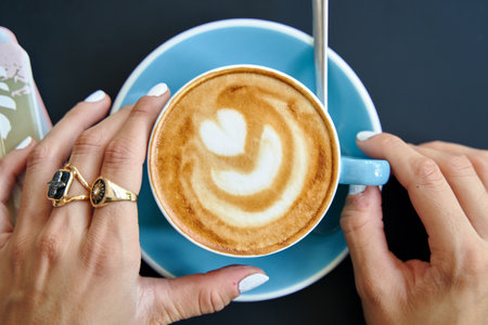 A top view of young female hands holding a cup of coffee latte with foam artの写真素材