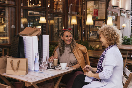 A shallow focus shot of two adult cheerful women with shopping bags having coffee and tea in a cafeの写真素材