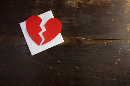 An envelope with a broken torn paper heart on top of it on a wooden backgroundの写真素材