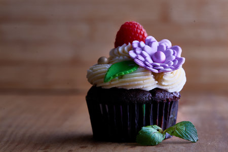 A closeup of a delicious chocolate cupcake, decorated with raspberry and handmade flower and leaf,...
