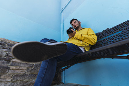A male using his camera while sitting by a blue wall