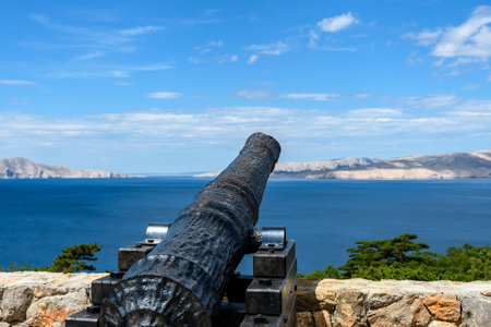 An old painted cannon pointing on a calm waveless sea under a cloudy skyの写真素材