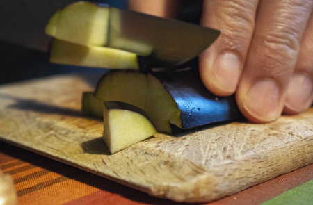 A closeup shot of a man cutting an aubergine on a wooden boardの写真素材