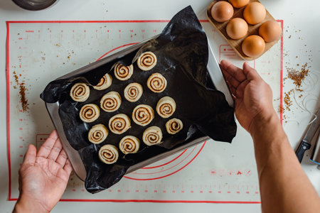 A man's hand holding a tray of cinnamon rolls ready to be put in the oven