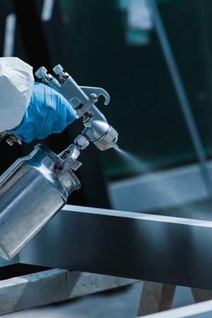 A vertical closeup of a person wearing a protective suit and gloves spraypainting in a workshop