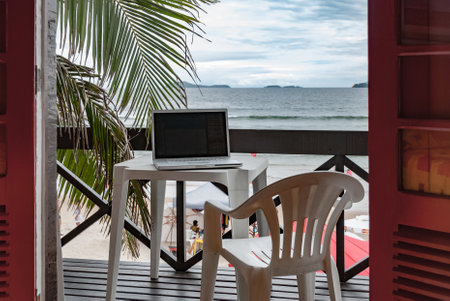 A laptop computer on a table in a tropical balcony near the sea-working from home vacation concept
