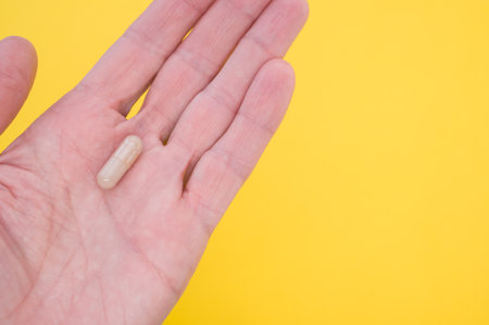 A capsule on a hand palm on yellow background with a copy spaceの写真素材