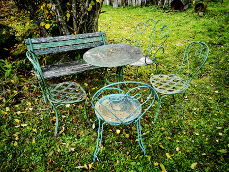 An old vintage metal garden furniture on a fresh grass lawn with fallen autumn leavesの写真素材