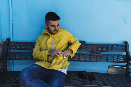 A closeup shot of a young man sitting on a bench in front of a blue wallの写真素材