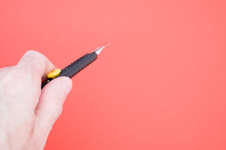 A hand holding a black snap-off blade knife on red background with a copy spaceの写真素材