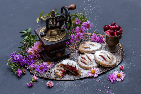 A closeup shot of bakery cookies with plums on a dark tabletop with pink flowersの写真素材