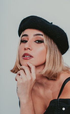 A portrait of a confident blonde female wearing a beret and a black denim jacket against a gray backgroundの写真素材