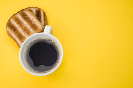 A high angle shot of a cup of coffee and toasts on a yellow surfaceの写真素材