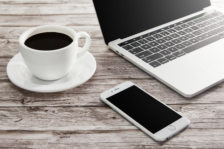 A high angle shot of a cup of coffee, laptop, and a smartphone on a wooden surface