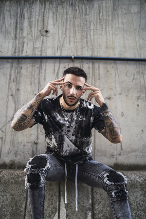 A hot tattooed stylish man wearing ripped jeans, a T-shirt with marble patterns and accessoriesの写真素材