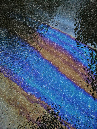 A closeup vertical shot of colorful gasoline fuel stain on asphalt pavement for abstract backgroundの写真素材