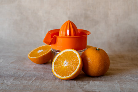 A selective focus closeup of a manual juicer surrounded with beautiful oranges on a beige background