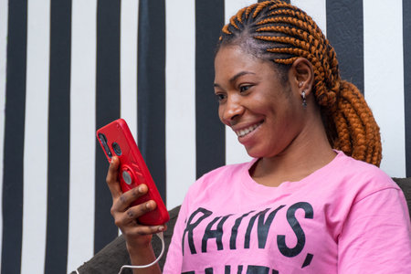 A young african lady smiling while using her phone that is charging.