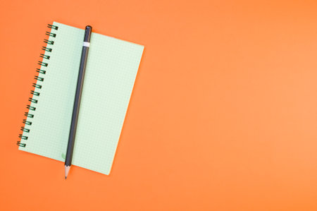 A top view of the green notepad and the black pencil on the orange surfaceの写真素材