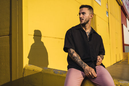 A young hot man wearing a black oversize shirt and pink pants sitting on yellow wallの写真素材