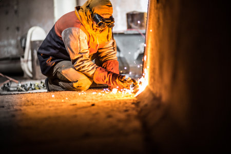 A demolition construction worker with full protective gear using a flame torch to cut up heavy...