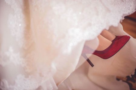 the red high heels of a wedding bride under the white wedding dressの写真素材