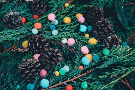 A closeup shot of evergreen tree branches and pinecones with small colorful pompomsの写真素材