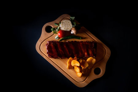 A top view of grilled beef ribs with vegetables on wooden board isolated on black backgroundの写真素材