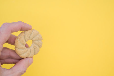 A hand holding a sun shaped cookie on yellow background with a copy spaceの写真素材