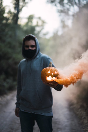 A vertical shot of a man holding a carved pumpkin with an orange smoke - the concept of Halloweenの写真素材