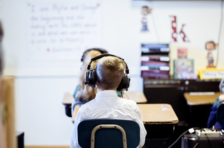 A selective focus shot of a kid wearing headphones sitting in the classroomの写真素材