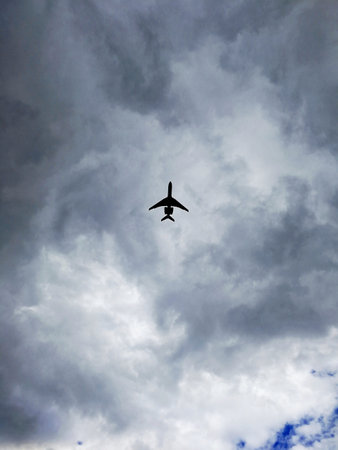 A low angle vertical shot of a silhouette of an aircraft flying in a heavily clouded rainy skyの写真素材