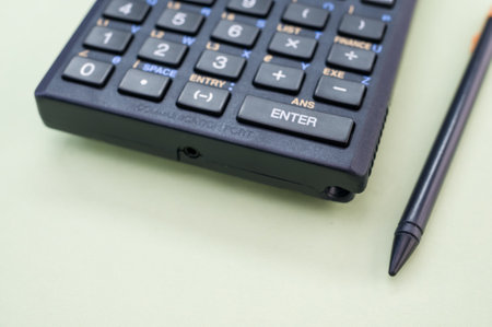 A closeup shot of a calculator and a pen on a green backgroundの写真素材
