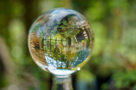 A closeup of a drop of water reflecting a metallic fence and a garden on blurred background